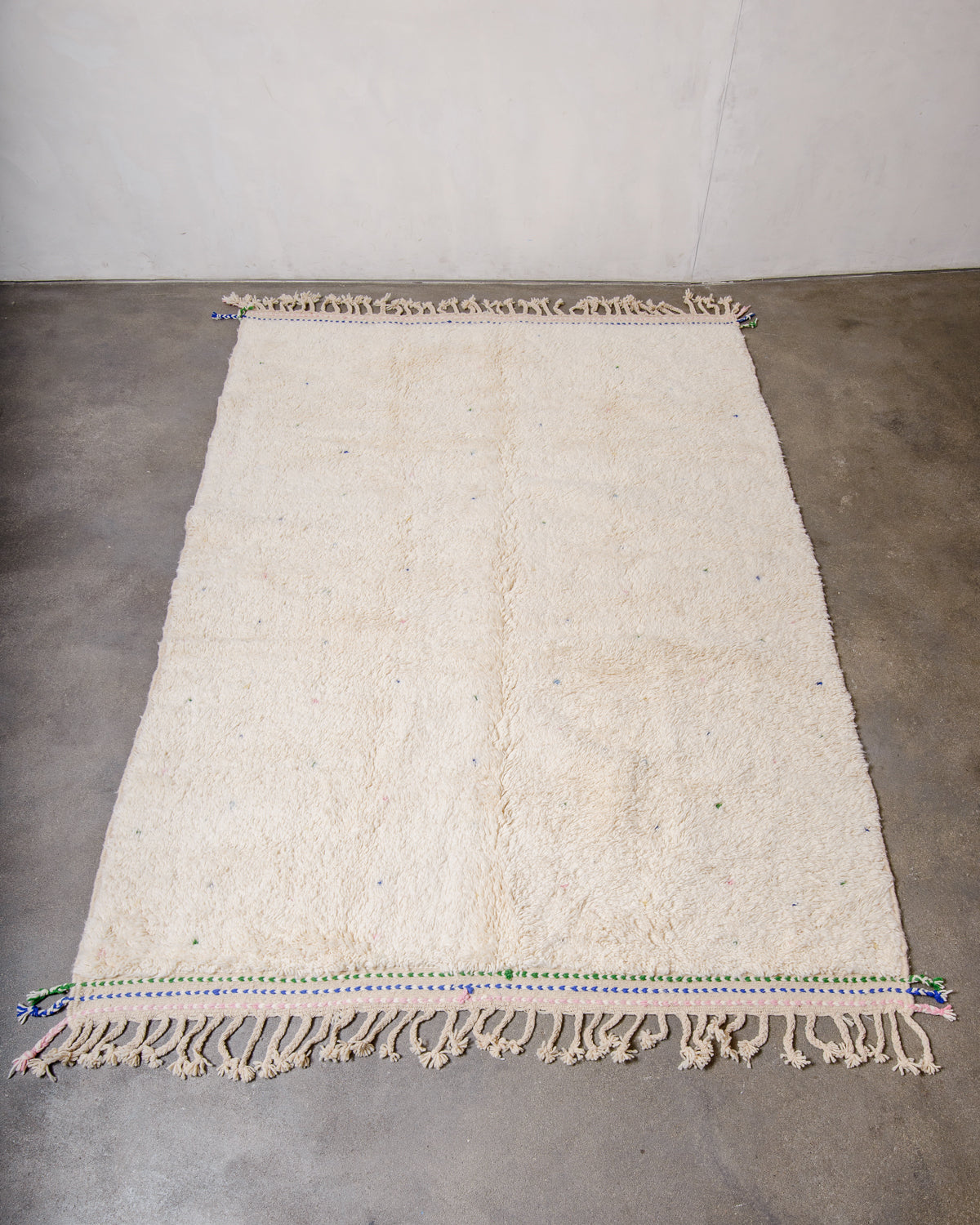 Berberlin Beniourain rug in cream wool with colourful dots laying on concrete floor.